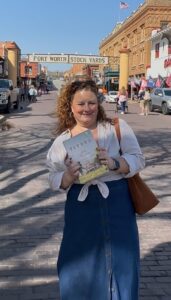 Jen at the Fort Worth Stockyards, 2025, holding Lila Meacham's book Titans, about early 20th Century cattle barons in Fort Worth.